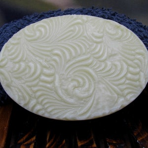 May include: A white oval-shaped bar of soap with a swirling, embossed pattern. The soap is sitting on a blue towel.