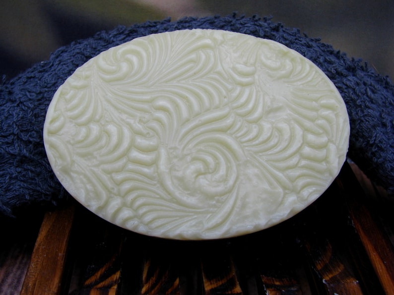 May include: A white oval-shaped bar of soap with a swirling, embossed pattern. The soap is sitting on a blue towel.