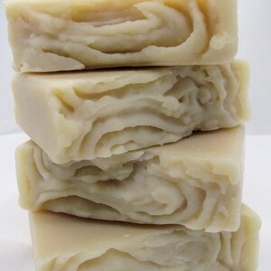 May include: Four bars of handmade soap stacked on top of each other. The soap is a light beige color and has a swirl pattern.