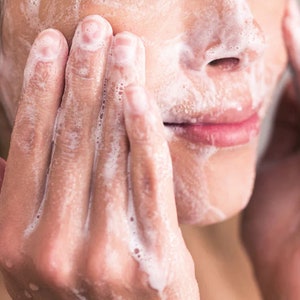 May include: Close-up of a person's face covered in white foam while washing their face.