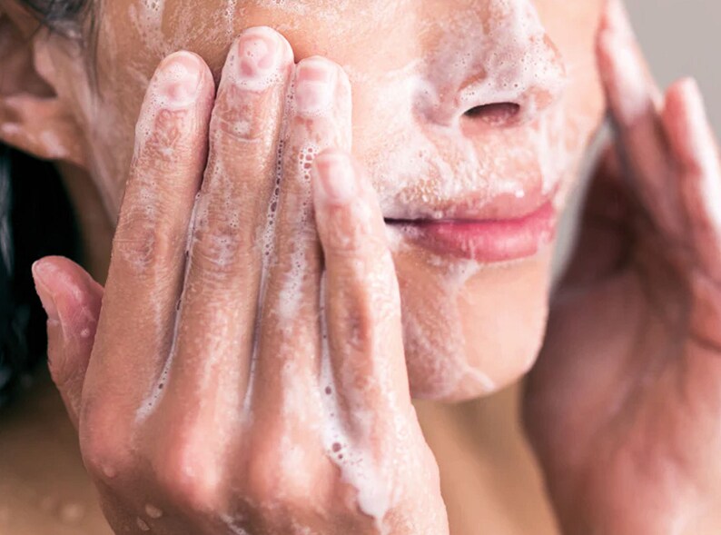 May include: Close-up of a person's face covered in white foam while washing their face.