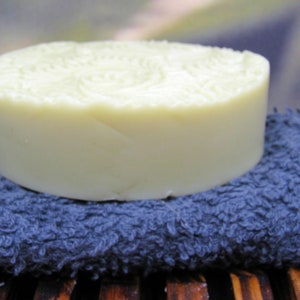 May include: A round, white bar of soap sits on a blue, textured towel. The soap has a swirl pattern on the top.