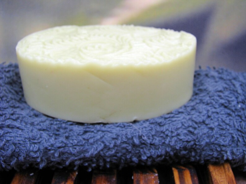 May include: A round, white bar of soap sits on a blue, textured towel. The soap has a swirl pattern on the top.