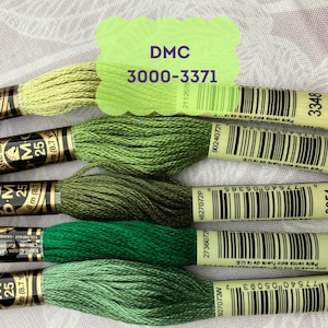May include: A collection of DMC embroidery floss in various shades of green. The image includes several spools of thread, each labeled with a number and barcode. A green label at the top reads "DMC 3000-3371".