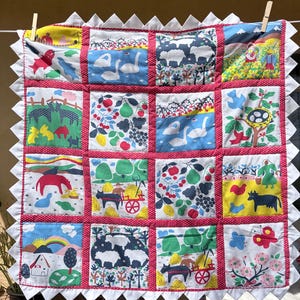 May include: A square patchwork quilt featuring sixteen distinct fabric panels with colourful illustrations of farm life, animals, and nature. The quilt is bordered by a white sawtooth edge and red polka-dot fabric strips between each square panel.