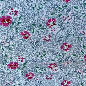 May include: Close-up of a fabric with a floral pattern. The design features pink and white flowers with red centers, green leaves, and gray stems on a white background. The fabric has a delicate, vintage aesthetic.