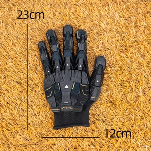 K&ouml;nnte beinhalten: Schwarz-goldener Handschuh mit futuristischem Design, 23 cm lang und 12 cm breit. Der Handschuh hat ein segmentiertes Aussehen mit einer schwarzen Manschette. Das Design beinhaltet geometrische Formen und goldene Details.