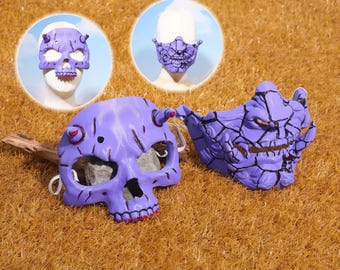May include: A collection of purple masks with a skull and demon theme. The masks have horns and intricate details, with a cracked texture. Two masks are displayed on a brown surface, with two additional masks in circular insets.