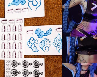May include: Sheets of temporary tattoos featuring blue cloud designs, bullet shapes, and gear-like graphics. The tattoos are on white backing sheets. The image also shows a person with blue hair and tattoos.