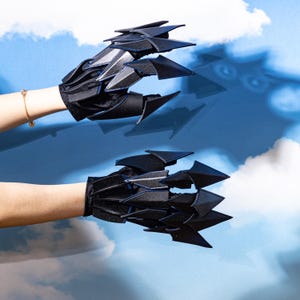 May include: Black claw gloves with sharp, angular blades extending from the knuckles and fingertips. The gloves are made of a dark, possibly velvet-like material, with a contrasting blue lining. The design suggests a costume or cosplay accessory.