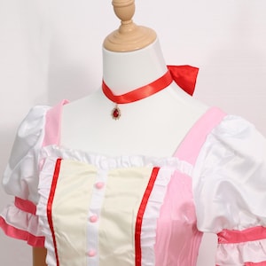 Detail shot of the accessories included with the Madoka Kaname cosplay set: matching gloves, pink choker with red gem, white socks, and decorative headwear. Each accessory is made to match the anime’s character design, offering a complete transformation into Madoka Kaname. Suitable for cosplay festivals, anime conventions, and as a gamer gift for fans of platform-style magical girl games. An excellent costume for collectors or performers.