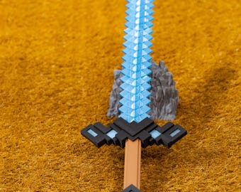 May include: A pixelated toy sword with a light blue blade and a brown handle. The hilt is black with light blue accents. The sword is set against a textured, golden-brown surface.