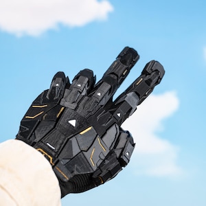 K&ouml;nnte beinhalten: Schwarzer und goldener Roboterhandschuh mit geometrischem Design, der ein Friedenszeichen vor blauem Himmel zeigt. Der Handschuh hat komplizierte Details und eine futuristische &Auml;sthetik mit goldenen Akzenten.