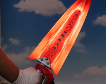 May include: A glowing red sword with a triangular blade and a detailed handle. The blade has a series of oval cutouts and a textured surface. The handle is red with silver accents and a purple gem. The sword is held against a blue sky background.