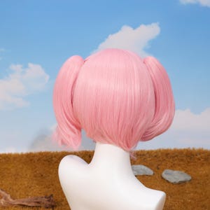 Close-up view of the Madoka Kaname pink twin tails cosplay wig showing the high-quality synthetic matte fiber texture and vibrant color. The wig is styled for anime accuracy, including parted bangs and curled twin tail tips. This heat-resistant wig is perfect for conventions, cosplay birthday gifts, holiday celebrations, platform gaming enthusiasts, and anyone looking to bring Madoka’s magical girl spirit to life.