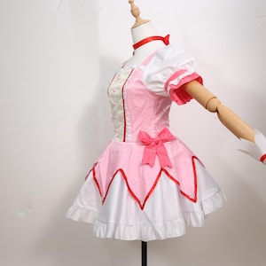 Madoka Kaname cosplay costume full set displayed on a mannequin, showcasing the complete magical girl outfit from the anime Puella Magi Madoka Magica. The outfit includes a frilly pink and white dress with puffed sleeves, red accents, and a layered skirt, along with matching gloves, socks, choker, and headwear. This costume is perfect for anime conventions, cosplay events, Halloween, or themed parties. Designed for comfort and screen-accuracy, it’s a popular choice for anime fans and gamers.