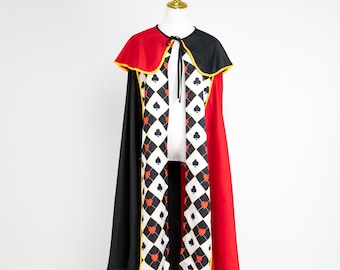 May include: A costume cape with a red and black design. The cape features a black collar with yellow trim, a red back, and a central panel with a diamond pattern of spades and hearts. The cape is displayed on a mannequin.