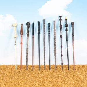 May include: A collection of eleven wands with varying designs and colors, including brown, black, and cream. The wands are arranged against a blue sky background with a brown textured surface, showcasing their unique shapes and details.