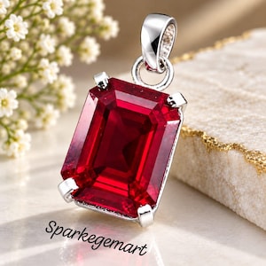 Peut inclure: Un pendentif rectangulaire en pierre rouge taille émeraude monté sur une monture en métal argenté avec quatre griffes et une bélière circulaire. Le texte Sparkegemart est imprimé en noir en bas à gauche du pendentif.
