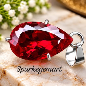 Peut inclure: Un pendentif en pierre précieuse rouge taillée en forme de poire, monté sur une monture à griffes en métal argenté avec une bélière assortie. Le mot Sparkegemart est imprimé en noir sous le pendentif, qui présente une couleur cramoisie.