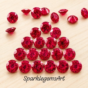 Könnte beinhalten: Eine Sammlung runder, im Brillantschliff geschliffener roter Edelsteine, die in einer dreieckigen Formation angeordnet sind, mit einigen losen Steinen darüber. Der Text SparklegemsArt ist unten im Bild schwarz aufgedruckt.