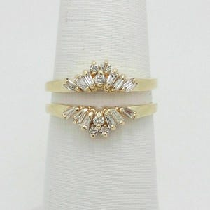 May include: A yellow gold ring guard set featuring two curved bands. Each band is adorned with a central cluster of small round diamonds flanked by tapered baguette-cut diamonds arranged in a fan-like pattern along the top edge of the gold band.