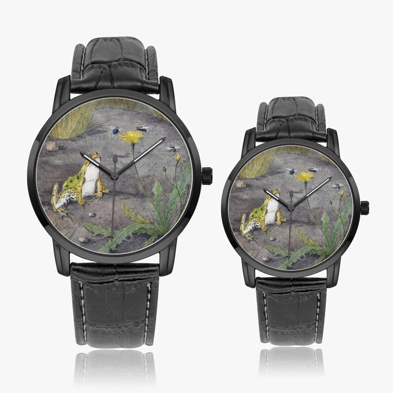 May include: Two black wristwatches with leather straps. The watch faces feature a detailed illustration of a frog, a dandelion, and insects on a stone surface. The watches have black bezels and hands.