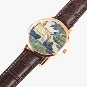 May include: A gold-toned wristwatch with a brown leather band. The watch face features a colorful painting of boats and buildings. The band is textured with white stitching. The watch is angled, showing the face and part of the band.