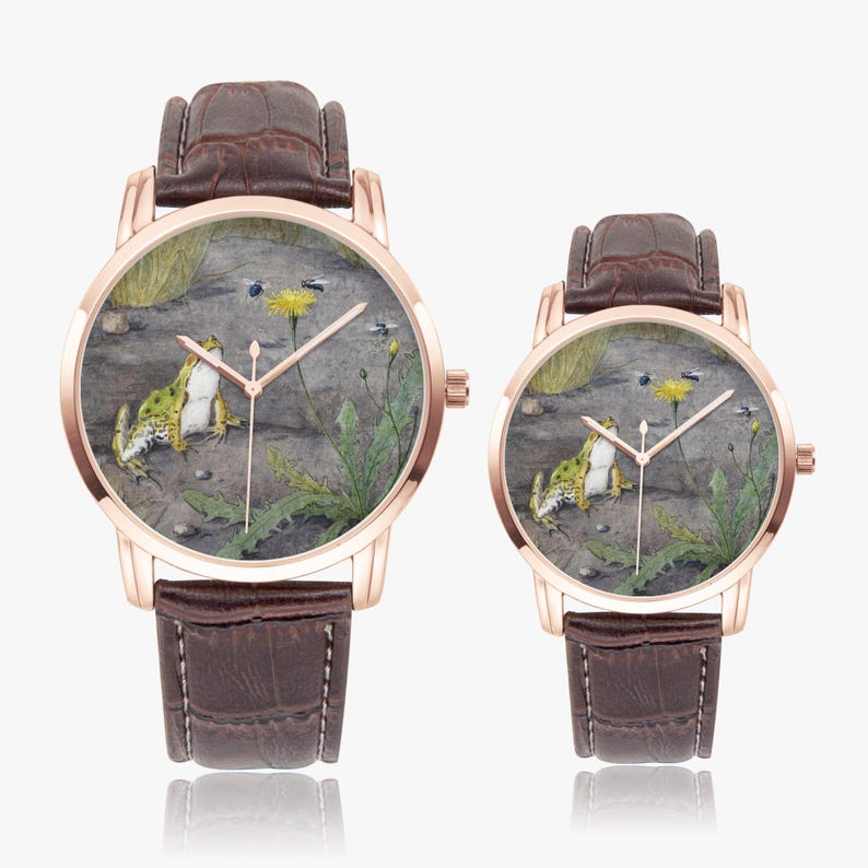 May include: Two rose gold watches with brown leather straps. The watch faces feature a detailed painting of a frog, a yellow flower, and insects. The watch hands are gold. The watches are displayed on a white background.
