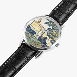 May include: A wristwatch with a silver-colored case and a black leather band. The watch face features a colorful painting of boats and a building. The painting has blue, yellow, and green hues. The watch has silver-colored hands.