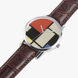 May include: A wristwatch with a silver case and a brown leather band. The watch face features a geometric design with red, black, yellow, beige, and blue blocks. The band has a crocodile skin texture.