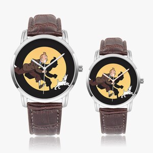 Op de afbeelding: Twee horloges met bruine leren bandjes en zilveren kasten. De wijzerplaten van de horloges tonen een cartoonafbeelding van een man, een hond en een gele achtergrond. De horloges worden weergegeven op een wit oppervlak.