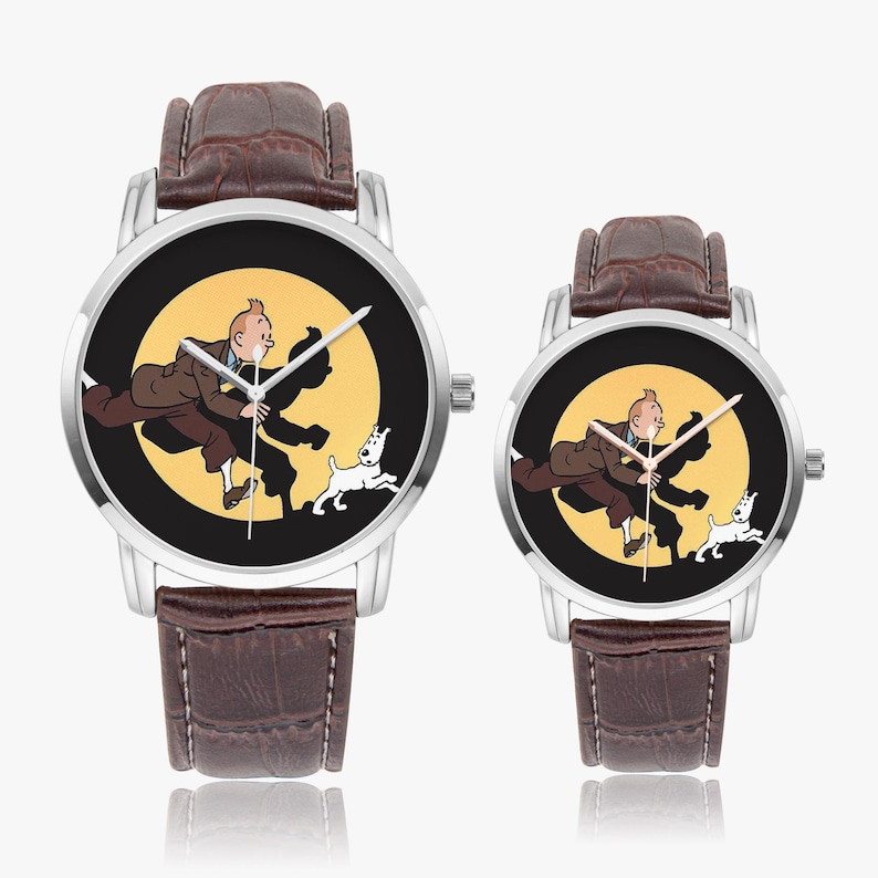 Op de afbeelding: Twee horloges met bruine leren bandjes en zilveren kasten. De wijzerplaten van de horloges tonen een cartoonafbeelding van een man, een hond en een gele achtergrond. De horloges worden weergegeven op een wit oppervlak.