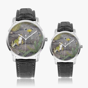 May include: Two watches with silver cases and black leather straps. The watch faces feature a detailed illustration of a frog, a yellow flower, and insects on a gray background. The watches are of different sizes.