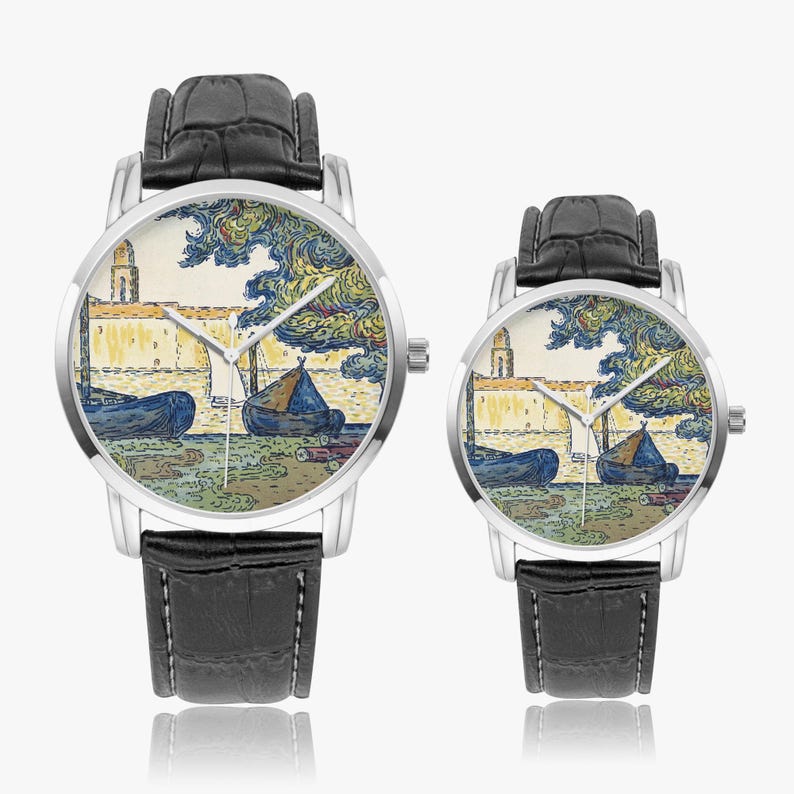 May include: Two silver-toned wristwatches with black leather bands. The watch faces feature a colorful painting of a coastal scene with boats and a building. The watches are displayed on a white background.