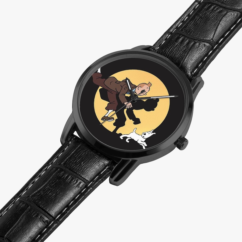 Op de afbeelding: Zwarte polshorloge met een cartoonillustratie van een man en een hond op een gele achtergrond. Het horloge heeft een zwarte kast en een zwarte leren band met witte stiksels. De wijzers van het horloge zijn zilver.