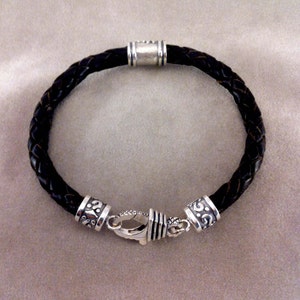 May include: A black leather bracelet with silver-toned clasps and decorative accents. The bracelet is braided and has a simple design.