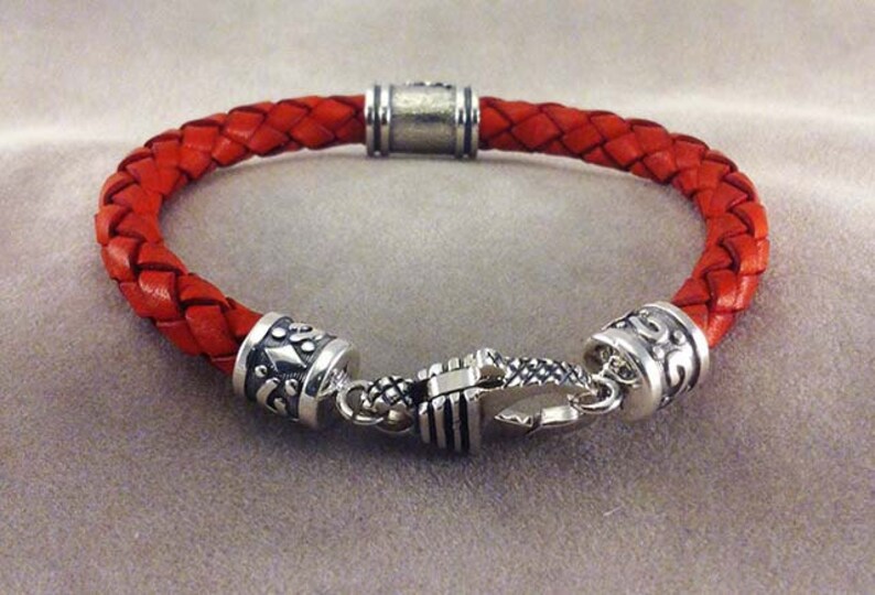 May include: A red leather braided bracelet with silver toned metal accents and a clasp closure.