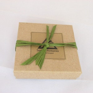 May include: A brown cardboard box with a green ribbon tied around it. The box has a label that says "Sen Antonio by Designer".