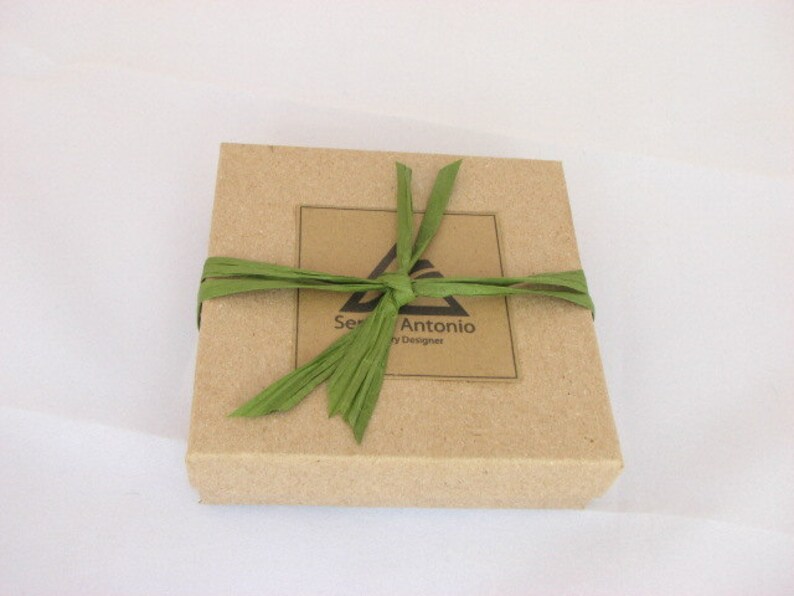 May include: A brown cardboard box with a green ribbon tied around it. The box has a label that says "Sen Antonio by Designer".