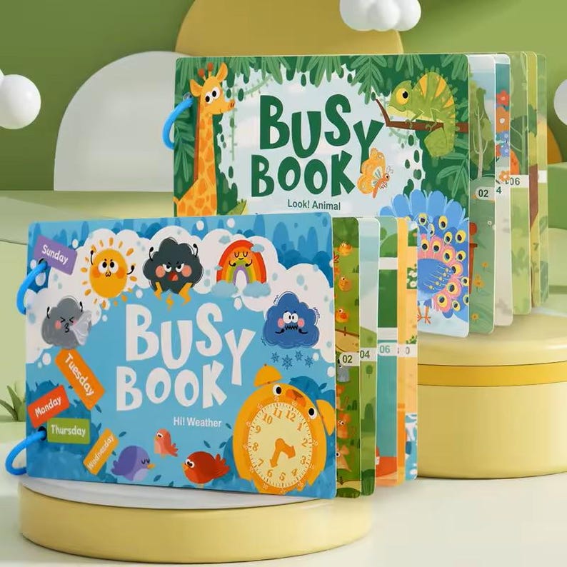 May include: Two children's "Busy Book" activity books. One book features a giraffe and the text "Look! Animal". The other book has a clock and the text "Hi! Weather". The books have colorful illustrations and are bound with blue rings.