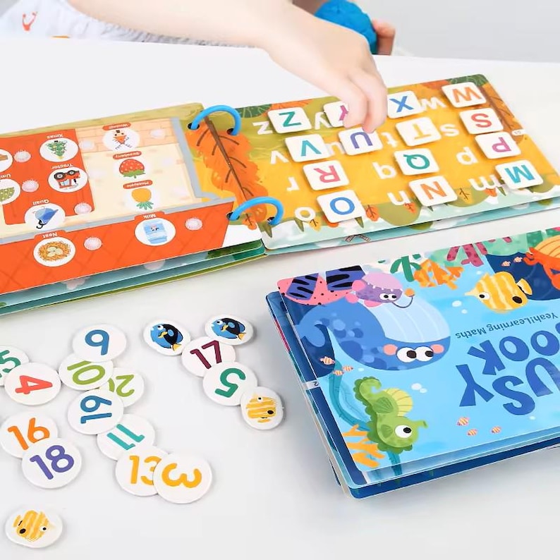 May include: A colorful educational toy set featuring a book with letters and illustrations, a book with a whale and fish, and number tiles. The set is designed for learning and play, with bright colors and engaging graphics.