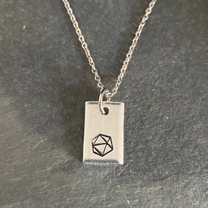 May include: A silver necklace with a rectangular pendant featuring a geometric design. The pendant is engraved with a black geometric shape.