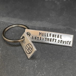 May include: Silver keychain with a small tag that says "Millennial Anti-theft Device" and a larger tag with a gear shift pattern.