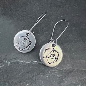 May include: A pair of silver earrings with a 20-sided die and a 1-sided die design.
