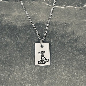 May include: A silver chain necklace with a rectangular pendant featuring a detailed engraving of a hammer.