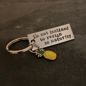 Hand stamped "I’m not inclined to resign to maturity" Psych inspired keychain with choice of pineapple charm