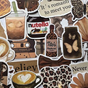 Puede incluir: Una colección de pegatinas con una paleta de colores cálidos y neutros. Las pegatinas presentan tazas de café con arte latte en forma de corazón, un tarro de Nutella, una botella de Tito's Handmade Vodka y diseños de mariposas y estampado de leopardo. El texto incluye "It's romantic to meet you" y "believe".