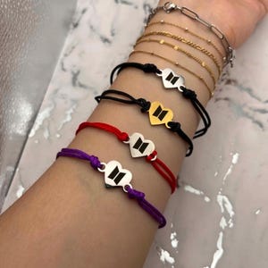 May include: Several bracelets with heart-shaped charms and a logo. The bracelets are in black, red, and purple. Other bracelets in gold and silver chain designs are also visible.