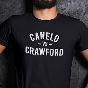 May include: Black t-shirt with the white text "CANELO -VS- CRAWFORD" in a bold, sans-serif font. The shirt is made of a soft material and has short sleeves. The text is centered on the chest.